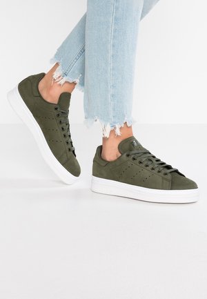Olivově zelené semišové tenisky s bílými gumovými podrážkami, kulatými šňůrkami, perforovanými bočními detaily a čistým, štíhlým silueta.