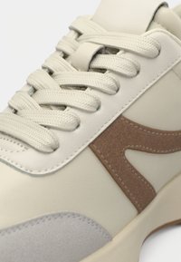 Λευκό αθλητικό παπούτσι με μπεζ σουέτ λεπτομέρεια, υφή γκρι πάνελ και φαρδιές κορδόνια. Ομαλή δερμάτινη επιφάνεια με ραμμένες λεπτομέρειες.