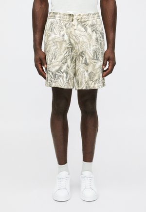 Herre shorts i let beige stof med et bladværk i grønne nuancer, med elastisk talje og snoretræk. Båret med hvide sneakers.