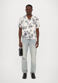 Kortærmet, cremefarvet skjorte med marineblå palmetræsmønster, parret med lyseblå slidte jeans. En sort taske og sko fuldender looket.