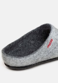 Pantofole grigie con fodera interna grigio scuro, caratterizzate da una suola nera e un dettaglio del logo rosso sul lato. Texture morbida e design semplice.
