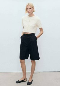 Vit fluffig crop-top med korta ärmar, parat med hög midja, skräddarsydda svarta shorts. Svarta slip-on flats fulländar outfiten.