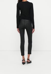 Top negro de manga larga con un escote redondeado, combinado con unos pantalones negros ajustados y unos zapatos de tacón negro de punta con una correa en el tobillo.