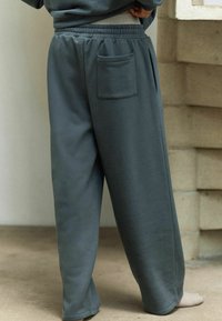 Pantalones de chándal grises hechos de una tela suave, con un corte relajado, cinturilla elástica y un bolsillo trasero.