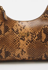 Brun slangeskindsprint håndtaske med en glat tekstur. Guld logo "GUESS EST 1981" på fronten. Har en lynlås og læderdetaljer.