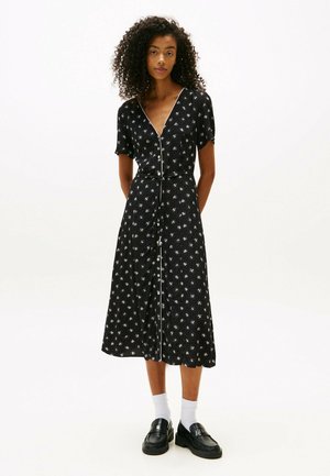 Vestido negro con estampado floral que presenta mangas cortas, escote en V y cierre de botones en la parte delantera. La tela tiene un ligero brillo y pequeños patrones de flores blancas.
