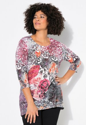 Haut à manches longues multicolore avec un col rond, présentant des motifs floraux et de crânes en rose, gris et orange sur un tissu texturé.
