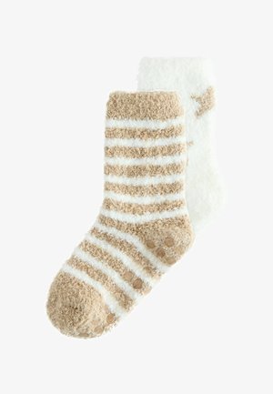 Un par de calcetines de tobillo esponjosos, uno beige con rayas blancas y puntos de agarre, el otro blanco con patrones de estrellas beige.