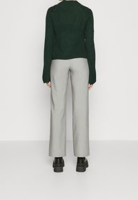 Pull en maille vert foncé à manches longues avec texture côtelée, associé à un pantalon large gris clair et des chaussures noires à semelle compensée.