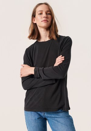 Maglietta nera a maniche lunghe realizzata in tessuto liscio, con scollatura rotonda e vestibilità comoda, abbinata a jeans blu.