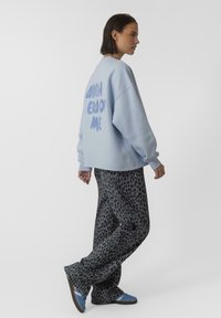 Jasnoniebieski, oversize'owy sweatshirt z napisem "CATCHER OF ME" na plecach; zestawiony z szerokimi, szarymi spodniami w leopardzi wzór i niebieskimi butami.