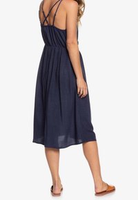 Námořnická modrá, bezramenné šaty s křížovými zadními popruhy, elastickým pasem a středně dlouhou sukní; lehká tkanina s texturovaným povrchem.