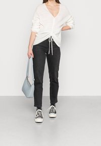 Weißer Strickpullover mit tiefem V-Ausschnitt und verstellbarem Kordelzug, kombiniert mit schwarzen Jeans und schwarz-weißen Sneakern. Hellblaue Handtasche.