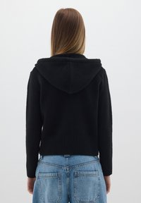 Felpa nera con cappuccio dal tessuto morbido, con polsini a coste e un design cropped, abbinata a jeans azzurri a vita alta.