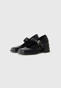 Black leather Mary Jane shoes with a low block heel and an adjustable buckle strap across the top.