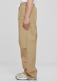 Beige, lichtgewicht, elastische taillebroek met een rechte pijpdesign, voorzien van zijzakken en een verstelbare zoom. Gecombineerd met neutrale sneakers.