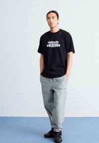Schwarzes T-Shirt mit kurzen Ärmeln und weißem Grafikdruck, kombiniert mit hellgrauen Jogginghosen, die einen elastischen Bund und Seitentaschen haben.