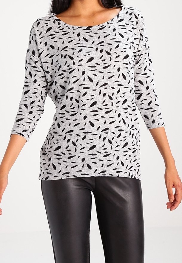 Haut gris à manches longues avec un motif de feuilles noir, présentant un col large et une coupe décontractée, associé à un pantalon en cuir noir.