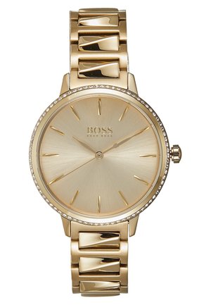 Gold Hugo Boss wristwatch with a round face, minimalist gold hour markers, slim hands, and a linked metal band with crystal accents.