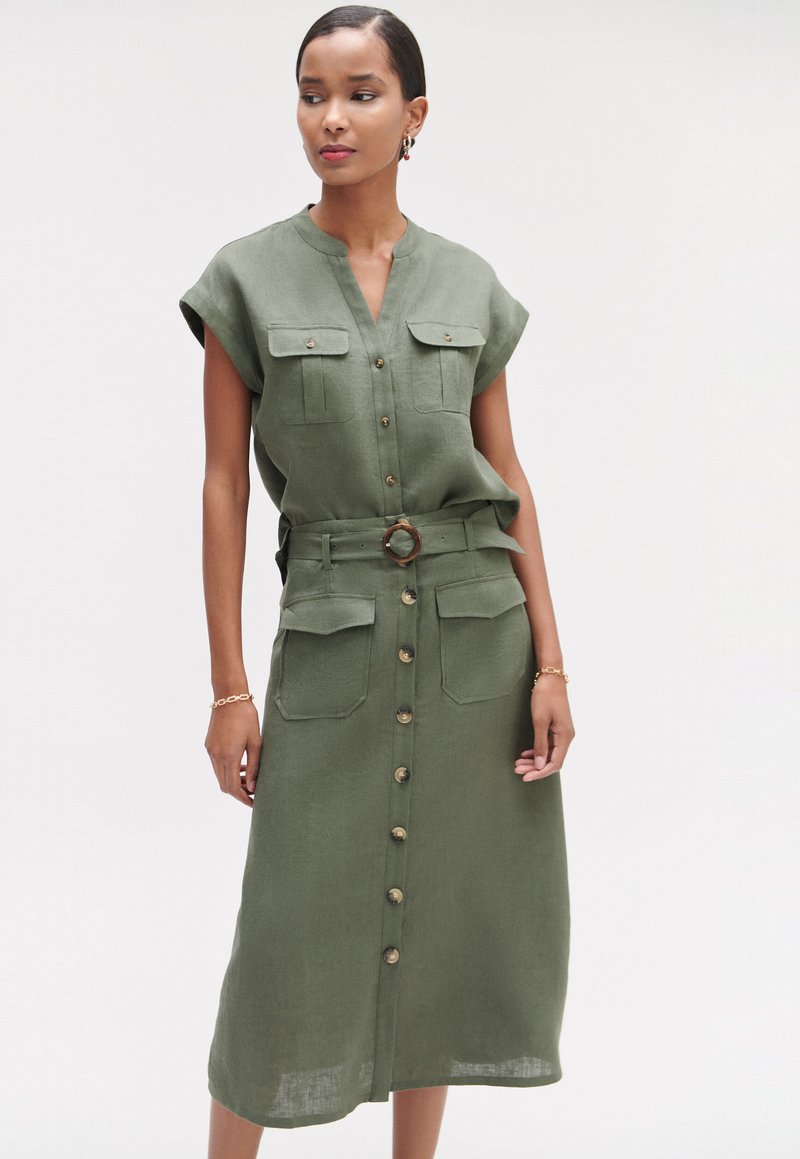 Vestido de lino verde caqui con mangas cortas, dos bolsillos en el pecho y un cinturón de tela a juego con un hebilla redonda; diseño de cierre con botones en la parte delantera.