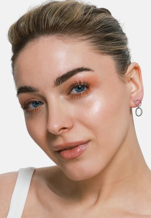 Silberne Creolen zeigen ein verdrehtes Design mit einem kleinen, glatten, runden Akzent. Die Ohrringe hängen zart an der Haut des Models.