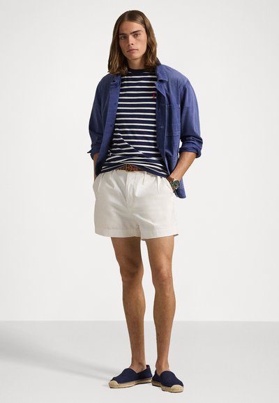 Neformálny outfit pozostávajúci z modrej košele na gombíky, pruhovaného trička v námorníckej modrej a bielej farbe, bielych šortkách a tmavomodrých espadrilkách.