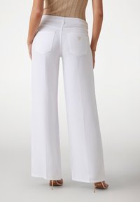 Pantaloni bianchi a gamba larga in denim con una texture liscia, dotati di due tasche posteriori e un piccolo logo accentato.