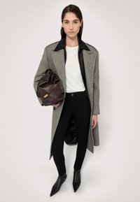 Grauer Wollmischungs-Mantel mit schwarzem Lederkragen, weißem T-Shirt, schwarzen schmalen Jeans und spitzen schwarzen Stiefeletten. Braune Lederhandtasche.