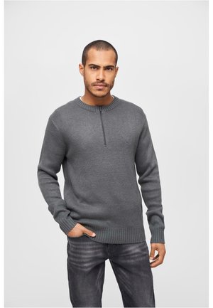 Suéter gris de punto con mangas largas, cuello alto y media cremallera. Cintura y puños acanalados. Combinado con jeans gris oscuro.
