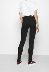Jeans skinny negros de cintura alta con una textura suave, silueta ajustada, bolsillos traseros, combinados con zapatillas blancas y burdeos, y una camiseta blanca holgada.