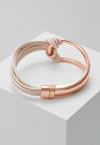 Armbands i roséguld med sammanflätade vita mjuka remmar, med en slät yta och en stilren, rundad design.