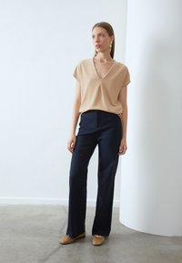 Beige, korte mouwen top met een V-hals; marineblauwe wijde broek; bruine flats; gladde textuur; minimalistisch ontwerp zonder patronen of accenten.