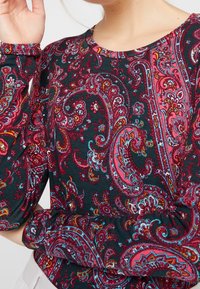 Long-sleeve top in dark fabric, featuring a vibrant paisley pattern with shades of red, blue, and white, textured with a soft finish.
