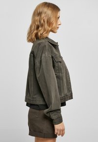 Khaki denim jacket featuring a classic collar, buttoned front, and two chest pockets. The design is slightly oversized with long sleeves.