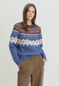 Pull en tricot avec une base bleue et des motifs géométriques multicolores, incluant des nuances de rose, d'orange et de crème. Manches et taille côtelées.