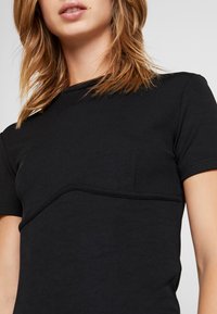 Camiseta negra de manga corta con un diseño acanalado, cuello redondeado y un sutil detalle de bolsillo en el lado izquierdo, confeccionada en tejido suave.