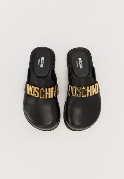 Μαύρα σανδάλια με επίπεδη σόλα, που διαθέτουν ένα έντονο χρυσό λογότυπο "MOSCHINO" κατά μήκος της επάνω λωρίδας. Λείο δερμάτινο υλικό.