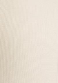 Tissu texturé en beige clair avec un motif côtelé subtil, mettant en valeur une surface lisse et douce, idéale pour des vêtements ou des accessoires.