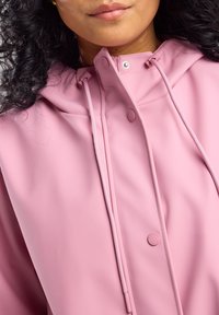 Pink waterproof jacket with a hood, featuring a smooth texture, snap buttons, and drawstring details for adjustable fit.