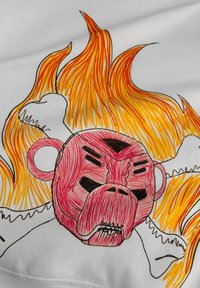 Witte stof met een rood en roze monster gezicht omringd door oranje en gele vlammen, getekend met dikke, gestructureerde lijnen.