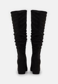 Bottes noires au-dessus du genou en daim doux, avec un design froissé, un talon bloc haut et une fermeture éclair sur le côté pour un ajustement.