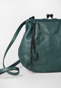 Taschen aus tealfarbenem Leder mit runder Form, ausgestattet mit einem Metallverschluss, einer Kettenakzentuierung und einem Silhouetten-Medaillon-Detail. Verstellbarer Riemen enthalten.