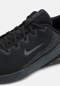 Scarpa sportiva nera con tomaia in rete testurizzata, dettagli TPU tonali e un distintivo logo a swoosh. Suola grigio scuro con grip in gomma.