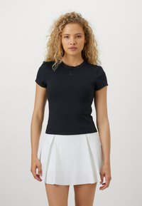 Haut noir à manches courtes ajusté avec un col rond et un logo subtil, associé à une mini-jupe blanche plissée. Texture lisse.
