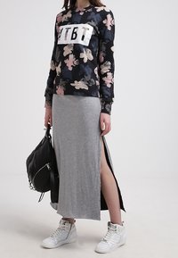 Černá mikina s květinovým potiskem a bílým logem, spárovaná s šedou maxi sukýnkou se bočními rozparky. Bílé tenisky a černá taška.