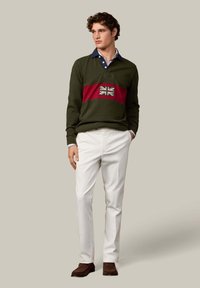 Zielona bluza z czerwoną paską i emblematem Union Jack, w połączeniu z białymi spodniami i brązowymi mokasynami. Projekt z warstwowym kołnierzem.