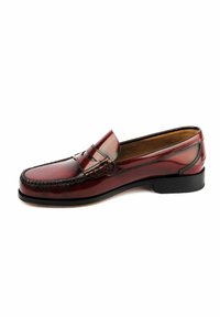 Mocasín de cuero marrón con un diseño elegante, punta redondeada y detalles cosidos a lo largo del borde. Suela negra baja. Acabado pulido.