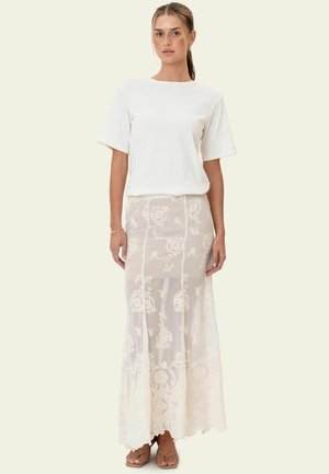 T-shirt blanc à manches courtes associé à une jupe longue beige transparente ornée d'une broderie florale blanche complexe et d'un design fluide et élégant.