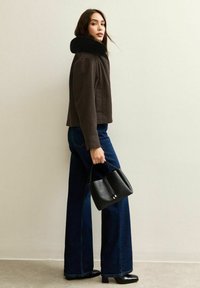 Bruine geruite cropped jack met een zwarte faux fur kraag, gecombineerd met flared blauwe denim jeans en een kleine zwarte leren handtas.