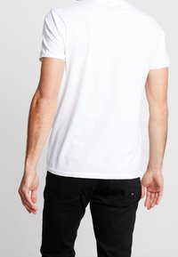 Hvid kortærmet t-shirt med rund hals, lavet af bomuld, med en glat struktur og en afslappet pasform, båret med sorte bukser.